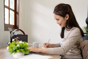 女人穿移动PC咖啡馆写作笔记有吸引力的女学生学习语言看在线网络研讨会听音频电子学习教育概念