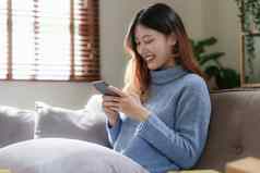 肖像年轻的亚洲女人聊天朋友检查社会媒体智能手机坐着沙发上生活方式概念