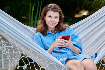 户外肖像十几岁的女孩坐着吊床智能手机