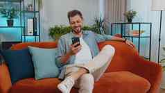 肖像年轻的男人。坐着沙发智能手机分享消息社会媒体应用程序