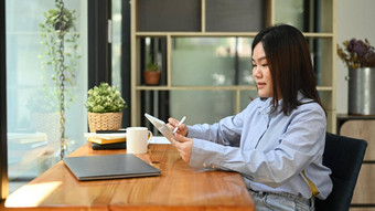 亚洲女人办公室工人蓝色的衬衫坐着工作场所窗口数字平板电脑