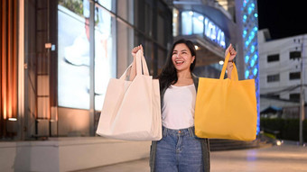 时尚女人购物袋站晚上城市街道黑色的星期五出售购物生活方式概念