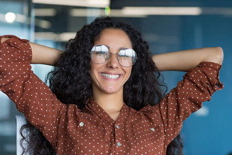 快乐年轻的女人企业家自由职业者工作现代办公室拉美裔眼镜卷曲的头发休息做白日梦办公室窗口微笑