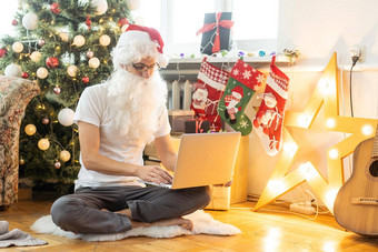 快乐圣诞老人老人西装坐着扶手椅移动PC圣诞节夏娃在线电子商务商店圣诞节假期在线出售概念背景圣诞节树花环墙