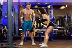 年轻的体育健身教练男人。火车年轻的美丽的女运动员健身房显示练习