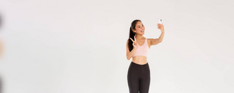 完整的长度可爱的亚洲健身女孩女运动员<strong>运动服</strong>装显示和平手势采取自拍移动电话女人锻炼健身房采取<strong>图片</strong>培训会话