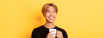 特写镜头快乐微笑英俊的金发碧眼的亚洲的家伙梦幻怀旧喝咖啡站黄色的背景