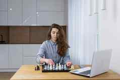 年轻的美丽的女人玩国际象棋在线移动PC研究教学坐着表格首页检疫