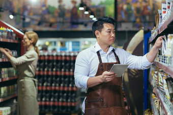 工人超市杂货店部门安排产品亚洲男人。平板电脑