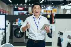 成功的销售顾问电子产品超市亚洲男人。工作电器商店微笑