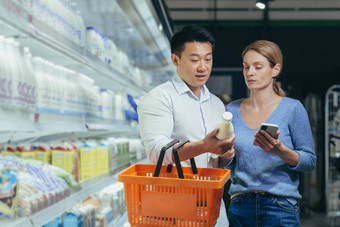 年轻的快乐亚洲夫妇智能手机超市购物车选择产品杂货店商店浏览聪明的电话快乐的每天食物购物列表人使选择选择