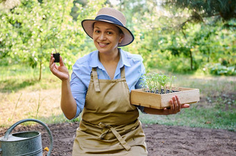 迷人的微笑中年女人农民持有木箱发芽幼苗树苗根地球