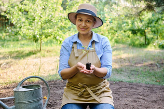 美丽的非洲美国女人农学家持有发芽幼苗番茄黑色的地球微笑相机