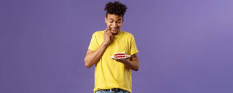 庆祝活动聚会，派对假期概念肖像的男朋友抵制诱惑吃一块蛋糕咬嘴唇微笑急切的咬甜点犹豫紫色的背景