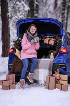 女人冬天衣服饮料热喝坐着车装饰一年的旅行车森林旅行圣诞节