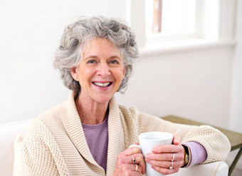 放松早晨津贴退休肖像高级女人持有杯咖啡坐着沙发