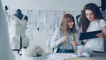 年轻的服装设计企业家看平板电脑选择织物颜色服装草图裁缝摇摇欲坠缝纫线程应用画