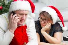 丈夫妻子一年的夏娃问题圣诞节男人。细胞电话担心女人有趣的圣诞老人老人帽子结婚了夫妇假期关注
