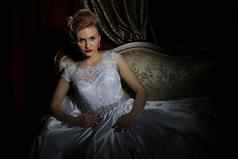 美丽的新娘白色衣服黑暗背景婚礼时尚沙龙华丽的新娘坐着豪华的沙发