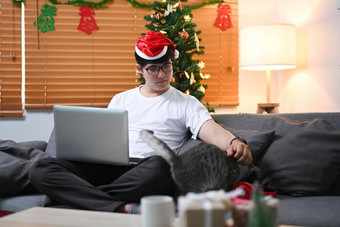 年轻的<strong>男</strong>人。圣诞老人他移动PC电脑坐着沙发可爱的猫圣诞<strong>节</strong>树<strong>首页</strong>