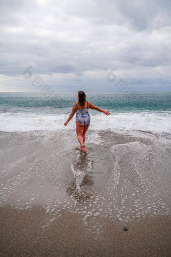 丰满女人洗澡西装进入水冲浪海滩灰色的天空云游泳冬天
