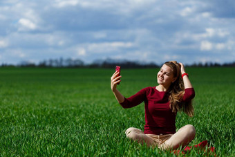 年轻的美丽的女人学生电话手坐着草女孩需要自拍需要自拍图片微笑享受温暖的一天概念照片智能手机