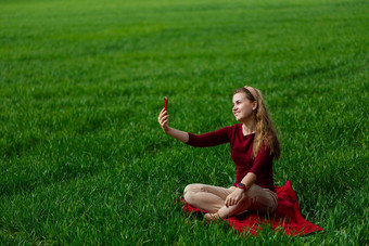 美丽的女人电话手坐在草女孩相机电话需要自拍照片微笑享受温暖的一天概念照片智能手机