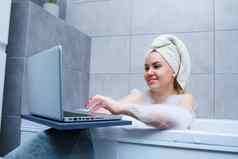 年轻的女人毛巾头看电影移动PC坐着浴美沙龙放松浴室亚麻身体护理放松概念