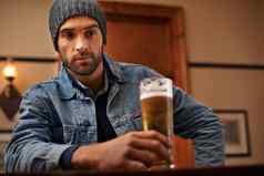 平静喝啤酒肖像英俊的年轻的男人。喝啤酒酒吧