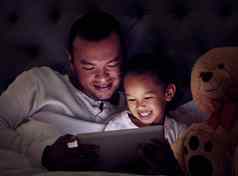 男人。孩子数字平板电脑流媒体电影卡通游戏床上晚上快乐父亲儿子浏览互联网在线网络社会媒体应用程序看喜剧卧室
