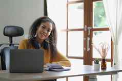 微笑年轻的非洲美国女人耳机心烦意乱电脑工作距离做梦快乐混血儿女研究在线首页移动PC思考规划愿景概念