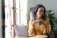 微笑年轻的亚洲女人移动PC网络相机持有杯咖啡穿耳机需房间首页
