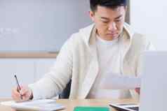 年轻的亚洲男人。文书工作首页坐着桌子上工作移动PC集中支付账单