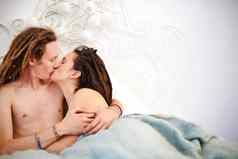 醒着的吻爱的年轻的夫妇接吻坐着床上