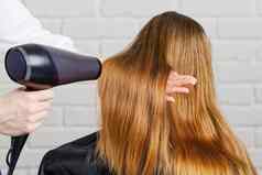 美丽的年轻的女人理发师打击干燥头发头发干燥机沙龙