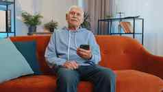 高级祖父坐着沙发智能手机分享消息社会媒体应用程序