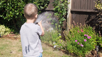有趣的男孩<strong>浇水草坪</strong>上植物花园住房后院可爱的孩子玩灌溉软管热阳光明媚的夏天在户外孩子们做家务活动孩子们童年
