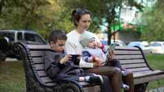 妈妈孩子们坐着板凳上公园充满激情的玩电话看漫画