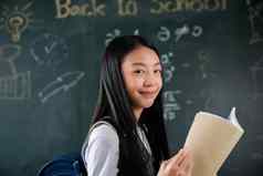 快乐美丽的亚洲女学生女孩站持有书站前面黑板上教室