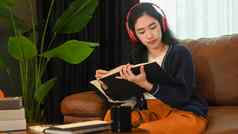满意年轻的女人听音乐耳机阅读书沙发上首页休闲活动积极的情绪概念