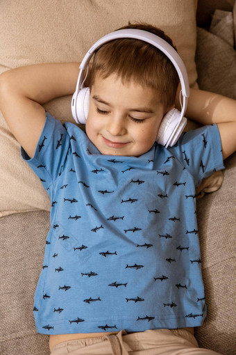 高加索人男孩蓝色的衬衫白色耳机听音乐音频书沙发上首页可爱的孩子放松休息房间