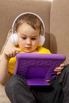 高加索人男孩黄色的衬衫玩游戏数字平板电脑首页肖像孩子首页看卡通紫罗兰色的平板电脑现代孩子教育技术