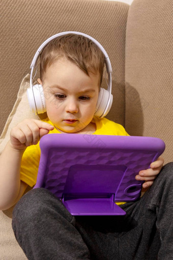 高加索人<strong>男孩</strong>黄色的衬衫<strong>玩游戏</strong>数字平板电脑首页肖像孩子首页看卡通紫罗兰色的平板电脑现代孩子教育技术