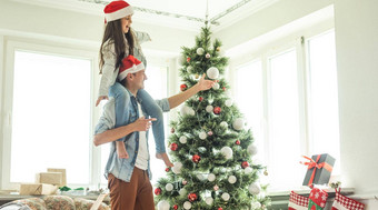 家庭装修圣诞节树年轻的男人。女儿肩膀帮助装修圣诞节树