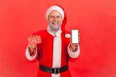 上了年纪的男人。灰色的胡子穿圣诞老人老人服装持有智能手机空白显示出售卡手折扣应用程序