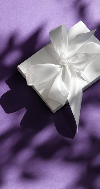 奢侈品假期白色礼物盒子丝绸丝带弓紫罗兰色的背景奢侈品婚礼生日现在