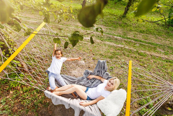 快乐妈妈。女儿放松吊床花园阳光明媚的夏天一天家庭玩吊床