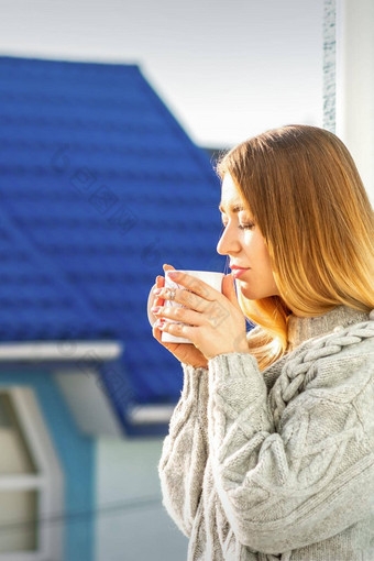 女人放松阳台咖啡美丽的年轻的女人毛衣持有杯咖啡站窗口早....