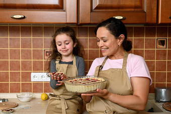 可爱的女孩持有烤樱桃馅饼坐着厨房计数器爱的妈妈