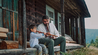 男孩爸爸玩木管乐器木长笛乌克兰索皮尔卡家庭二重唱人音乐概念父亲儿子传统的绣花衬衫坐着玄关木房子